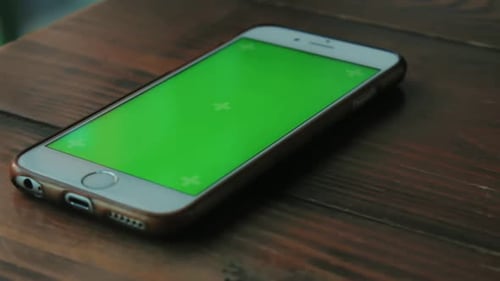 White Phone with a Green Screen Is on a Dark Brown Wooden Table in a Cafe