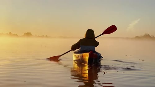 Kayaker Floats on Calm Water Through the Morning Fog Above the Water at Sunrise the Silhouette of a