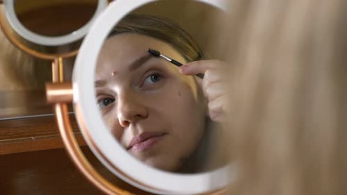 Woman Brushes Eyebrows in Front of Vanity Mirror