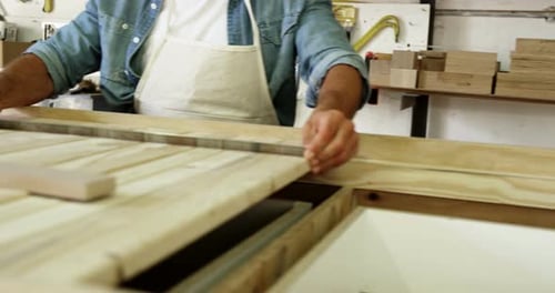 Carpenter Measures Wood at Workbench in Workshop