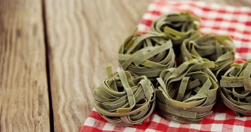 Roll of green tagliatelle pasta with red and white checks napkin on wooden table background