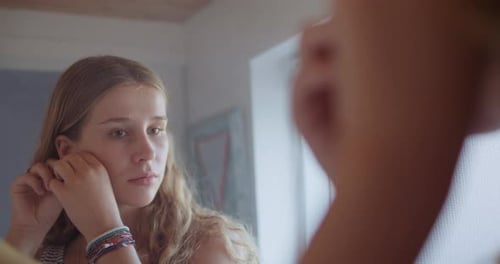 Young Woman Puts on Earring in Mirror