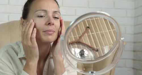 Woman Massaging Face in Mirror in Natural Light