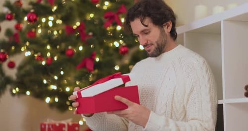 Man Opening Christmas Gift Near Tree in Home