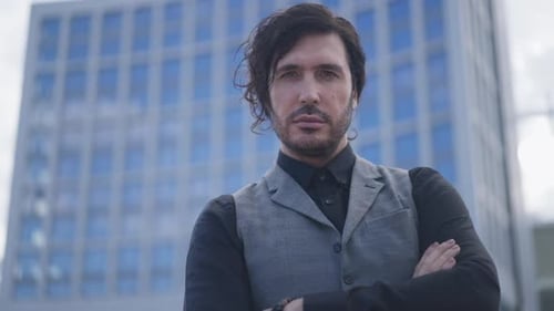 Elegant Handsome Man Crossing Hands Looking at Camera Standing at Urban Skyscraper Outdoors