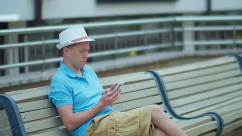 Young Man Sitting on a City Bench with a Mobile Phone in His Hands Camera Tracking
