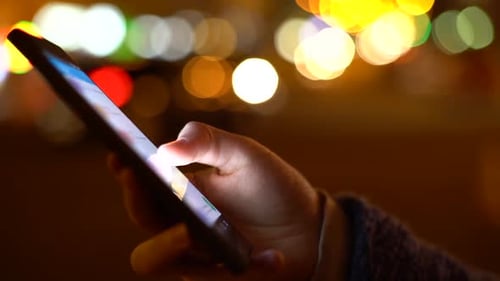 Hand Using Smartphone at Night with Bokeh Lights