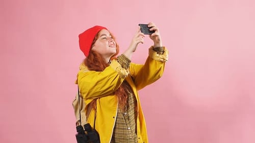 Studio Portrait of a Tourist Girl in a Yellow Cloak Photographing Nature on a Smartphone.