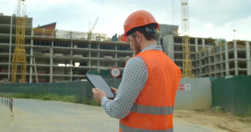 Close-up Portrait of Engineer with Gadget on Background of Building Under Construction. Modern