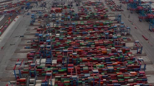 Luftaufnahme von Reihen bunter Frachtcontainer im großen Industriehafen, die automatisiert bewegt werden