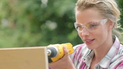 Woman Using Power Drill on Wood Outdoors