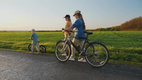Woman with Children Walking Along the Road Holding Bicycles in Their Hands