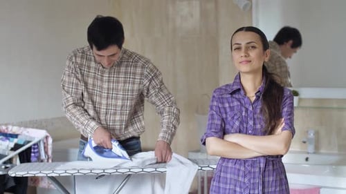 Man Ironing Shirt While Woman Smiles at Camera