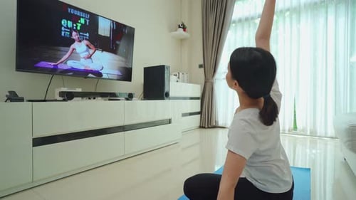Hermosa joven asiática sigue el vídeo de entrenamiento deportivo para hacer ejercicio en casa viendo un entrenador en línea.