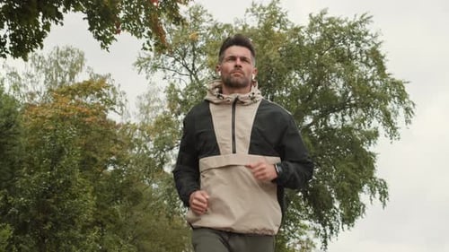 Caucasian Sportsman Jogging and Listening to Music in Park