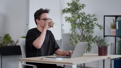 Young Man Works on Laptop, Drinks Coffee
