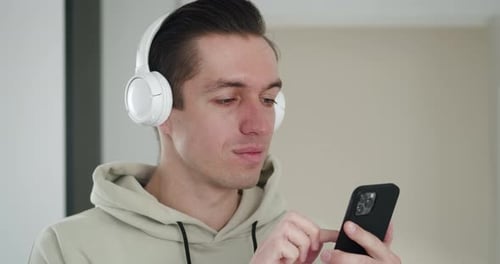 Man With Headphones Scrolls on Phone and Smiles