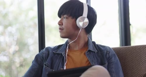 Happy young Asian man listening for music with headphone in living room.