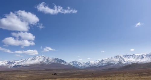 Timelapse of Sun Movement on Crystal Clear Sky with Clouds Over Snow Mountain Top. Yellow Grass at