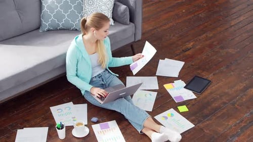 Young woman works with documents using a laptop at home.