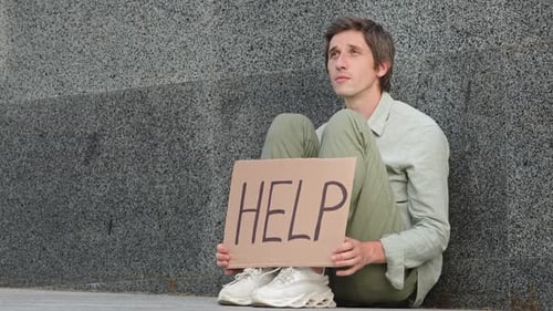 Sad Hopeless Young Man Sitting Outdoors with Sign Banner Announcement Help Victim of Disaster