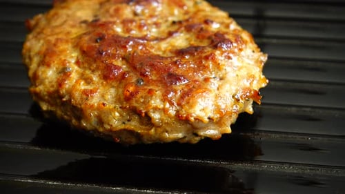 The fried cutlet for hamburger rotates on the grill pan.