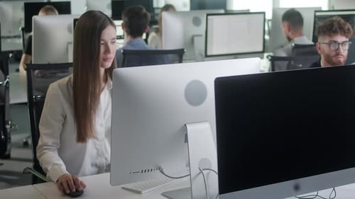 Attraktive junge Frau arbeitet am Decktop-Computer, während sie im großen Open Space Office arbeitet