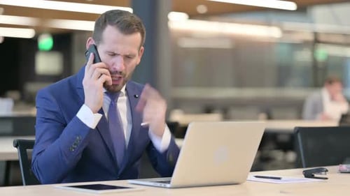 Serious Man Talking on the Phone at Office Desk