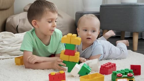 Little Boy Teaching His Baby Brother Building Tower with Toy Blocks and Bricks