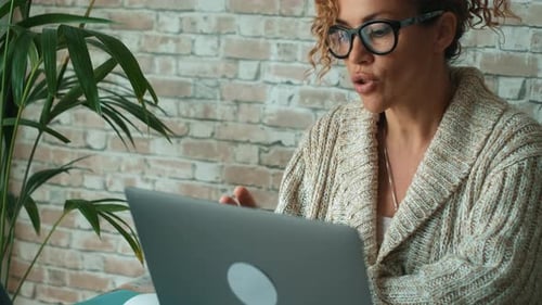 Woman Talking Using Laptop in Front of Brick Wall