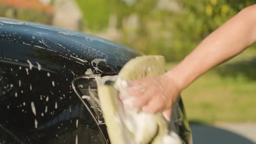 Manual washing of a black car headlight, front side view