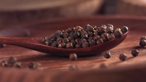Black Peppercorns Falling Onto Wooden Spoon