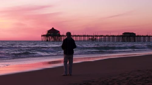 Man Watching Beach Sunset with Distant Pier