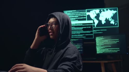 Un jeune hacker asiatique utilise le piratage informatique et parle au téléphone