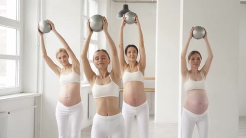 Gruppe junger schwangerer Frauen in Sportbekleidung, die Übungen mit Fitnessbällen machen