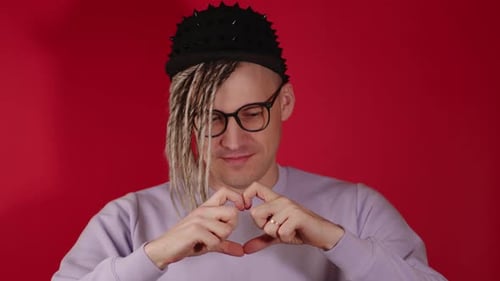 Young Adult Makes Heart Shape Gesture on Red