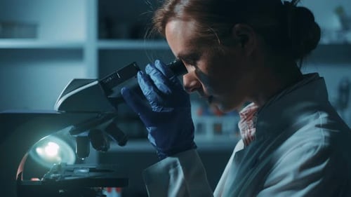 Woman Scientist Uses Microscope in Dark Lab
