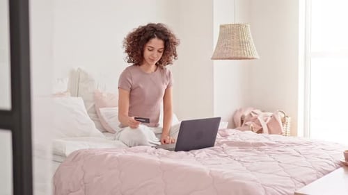 Woman Sits on Bed Using Laptop and Credit Card