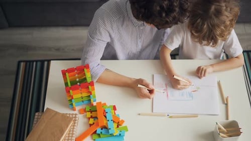 Kleines Kind beim Zeichnen und Ausmalen von Bildern mit vorsichtiger Mutter am Tisch zu Hause
