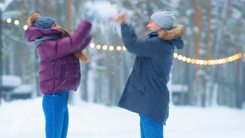 Un couple drôle en vestes et chapeaux jette de la neige dans un parc d'hiver