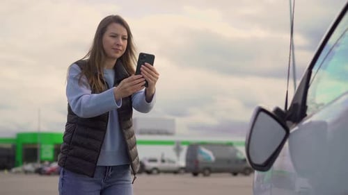 Young Woman Using Phone Near Car in Parking Lot