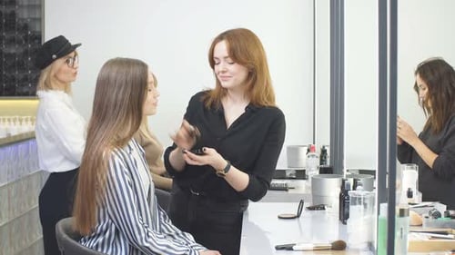 Beautiful Caucasian Client Sitting in Hair Salon While Hairdresser Is Combing Her Long Hair.