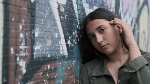 Young Beautiful Girl Standing Near the Wall with Graffiti and Posing Looking at the Camera with a