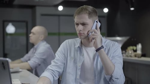 Handsome Concentrated Man Talking on Phone and Surfing Internet on Laptop