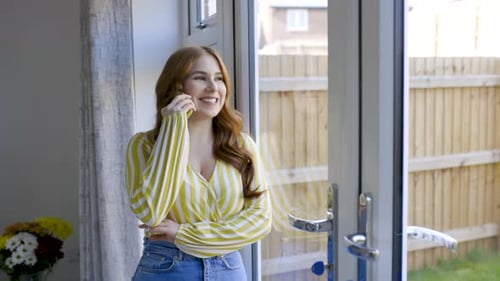 Smiling woman leaning on glass door, talking on the phone