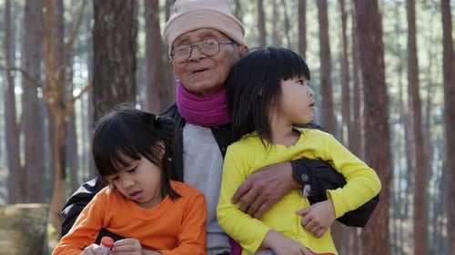 Asiatischer Großvater entspannt sich mit Enkelkindern in einem Campingurlaub im Pinienwald.