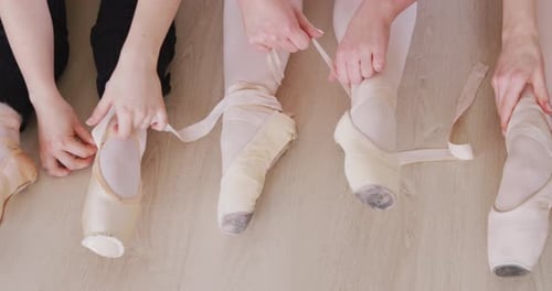 Danseuses de ballet caucasiennes assises ensemble sur le sol et discutant tout en attachant des chaussures de ballet