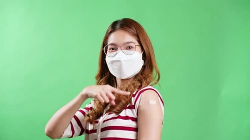 Young Asian woman pointing to her arm after being vaccinated against covid-19 in studio with chroma