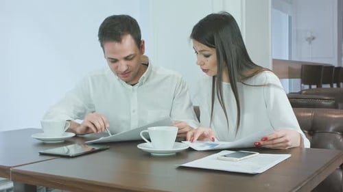 Two Business Partners Discussing Work and Smiling While Sitting in Cafe