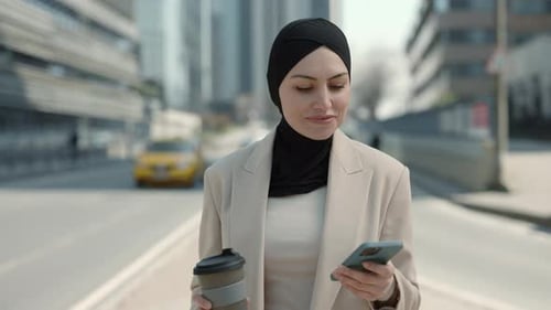 Woman in Hijab Using Mobile and Drinking Coffee Outdoors